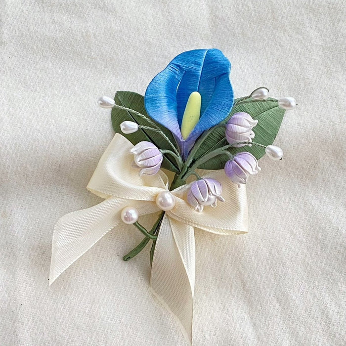 Handmade Chanhua floral arrangement brooch with blue calla lily purple bellflowers, cream ribbon and pearl accents on neutral fabric background