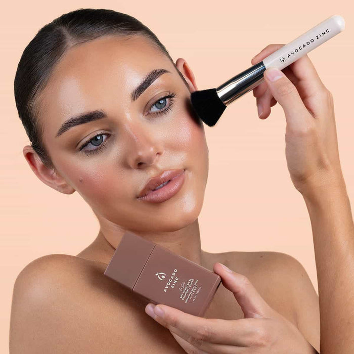Woman applying makeup with a brush and product container against a beige background