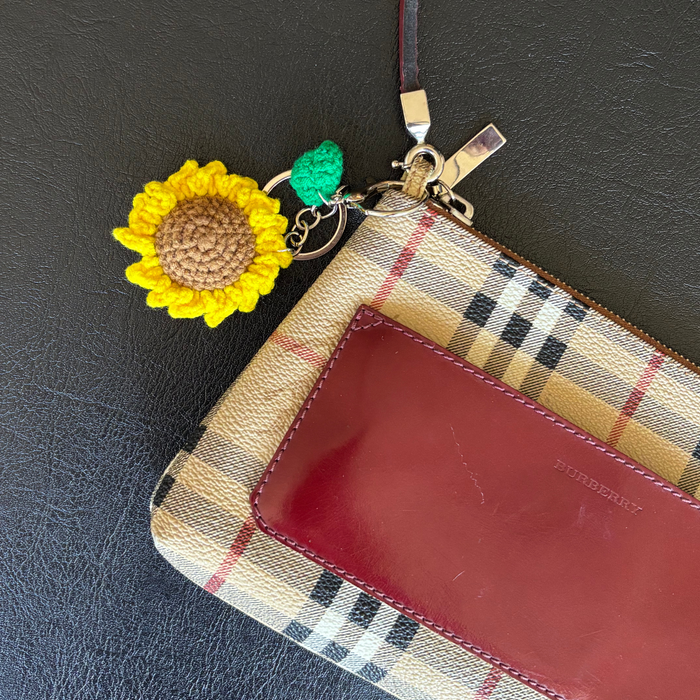 Burberry plaid pouch, red cardholder, and yellow sunflower bag charm on a black surface.