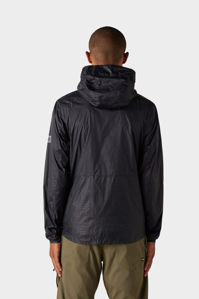 A person stands with their back to the camera, wearing the 686 Mens Grid Shell Jacket in black by 686 and olive green pants, set against a plain light gray background.