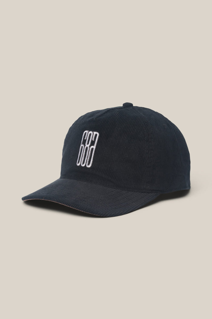 The 686 Mid-Pro Ghost Cord Unstructured 5 Panel Hat by 686 is a navy blue corduroy polyester-cotton woven men’s baseball cap, featuring white embroidered geometric lines on the front, displayed against a plain beige background.
