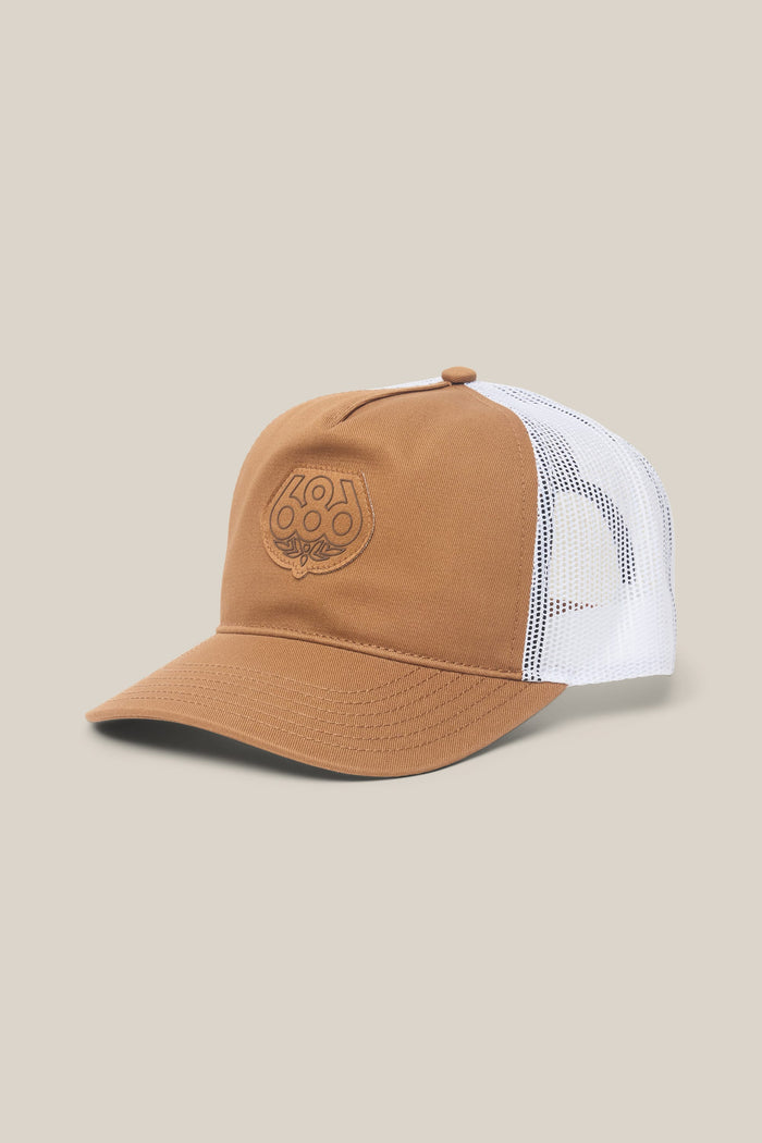 The 686 Mid-Pro Wreath Unstructured 5 Panel Mesh Hat by 686 is a brown and white men's trucker-style hat made from polyester cotton woven fabric, featuring a mesh back, curved brim, and an embroidered logo on the front. The background is plain beige.