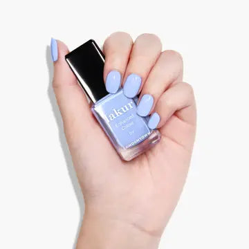 A hand with light purple nail polish, featuring a subtle blue tone, holds a matching bottle of LONDONTOWN Amalfi Love nail polish against a white background.
