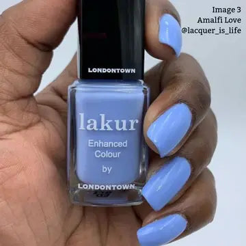 A hand with short nails painted cool blue holds a bottle of LONDONTOWN Amalfi Love nail polish, the perfect shade for beach vibes.