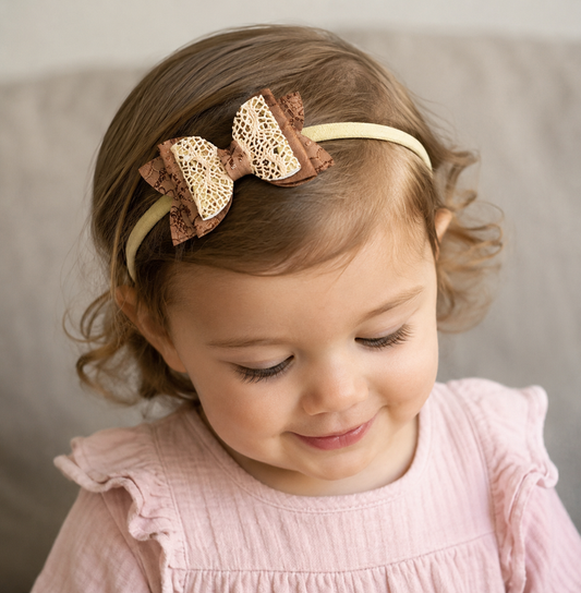 Child wearing a pink and gold headband with a bow on a neutral background