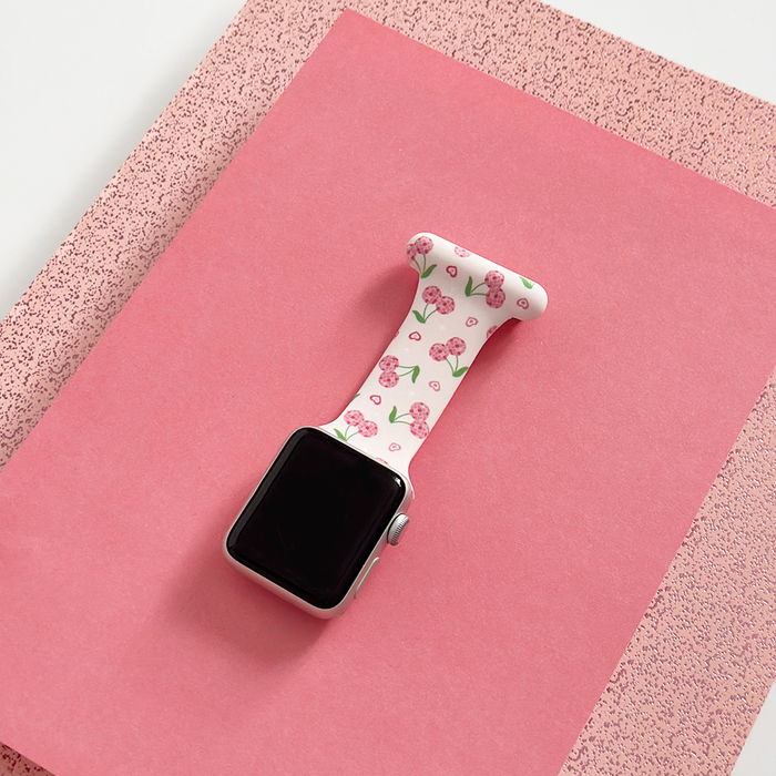 Coconut Lane Apple Watch clip-on fob strap with red cherry pattern on pink, shown on pink and speckled paper backgrounds.