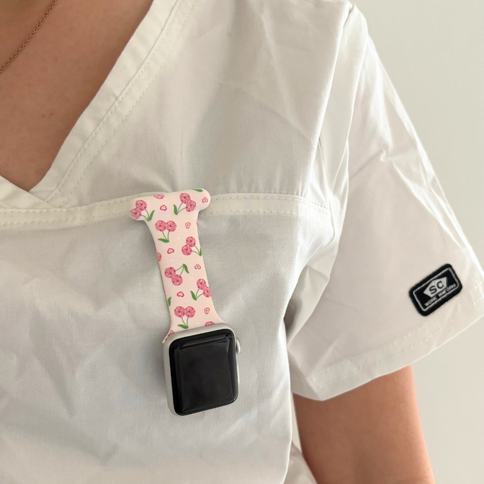 White scrubs with a colorful Disco Cherries Apple Watch clip-on fob strap clipped to the chest pocket.