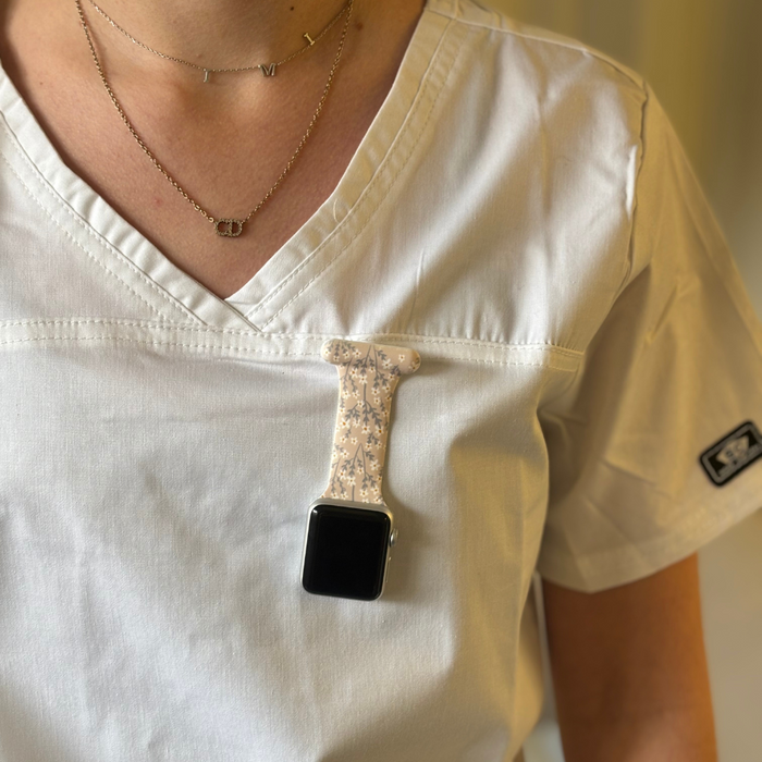 Apple Watch clip-on fob strap with a nude floral pattern attached to white scrubs.