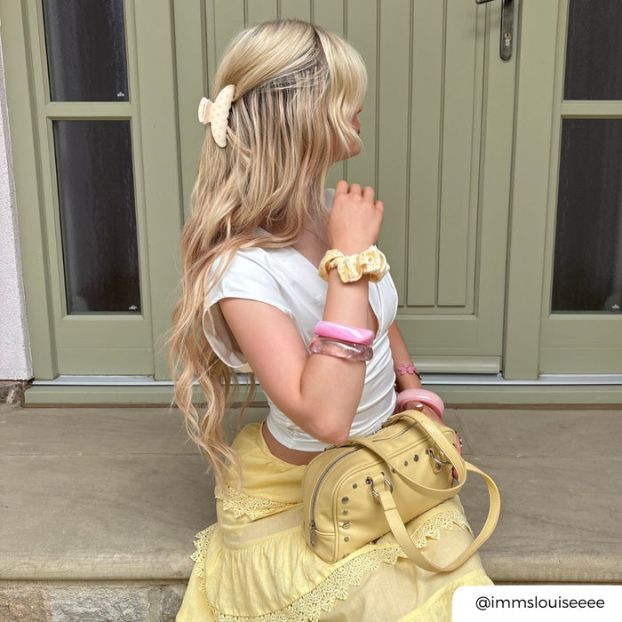 butter blush claw clip in hair with scrunchie on wrist and yellow handbag with matching bangles.