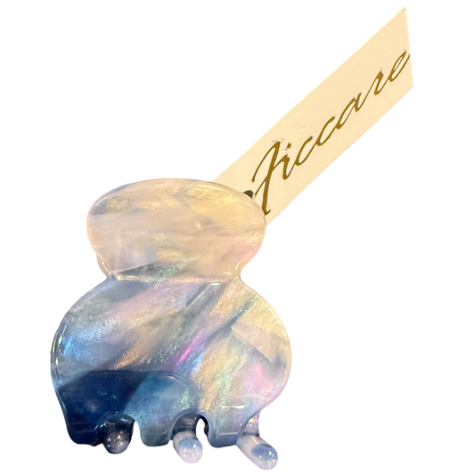 An iridescent jelly hair claw clip with a double-bulb design, featuring a holographic finish that shifts between blue, purple, and gold. A beige paper tag with the brand name 'Piccare' in gold script is attached to the clip, set against a plain white background.