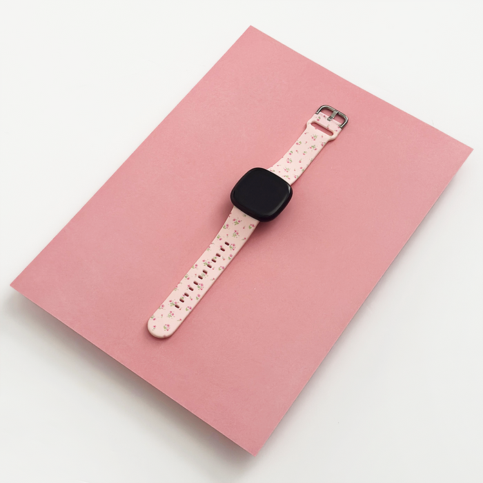 Pink floral Coconut Lane Fitbit strap on a matching pink rectangular surface.