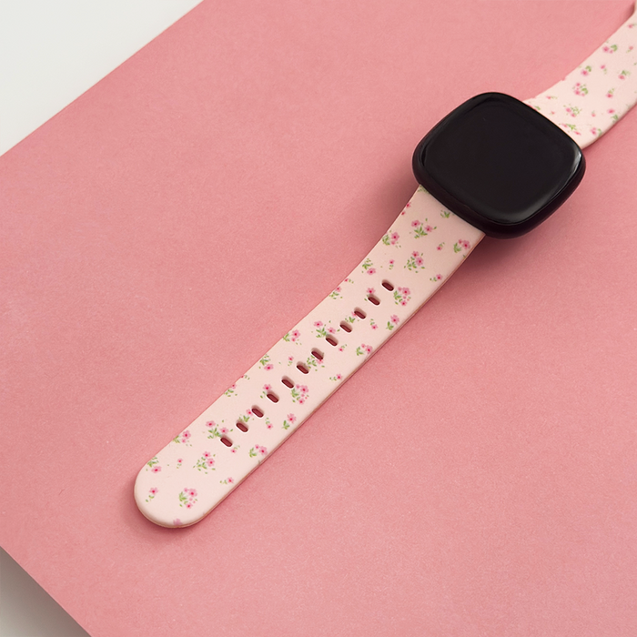Pink ditsy floral Coconut Lane Fitbit strap displayed with a smartwatch on a pink background.