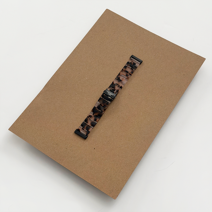 LUXE Ivory Tort Coconut Lane Fitbit strap with a tortoiseshell pattern on brown cardboard, white background.