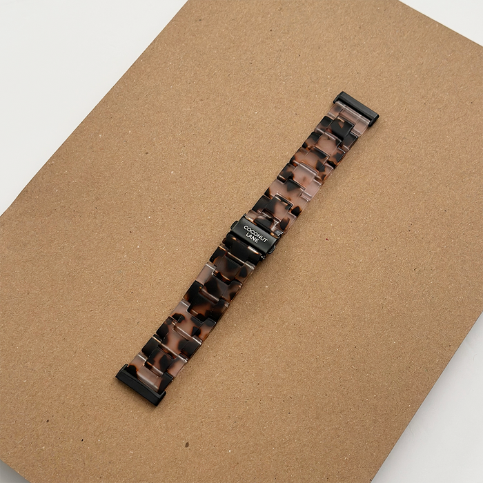 Ivory tortoiseshell Coconut Lane Fitbit Luxe strap with black clasp, shown on a brown textured surface.