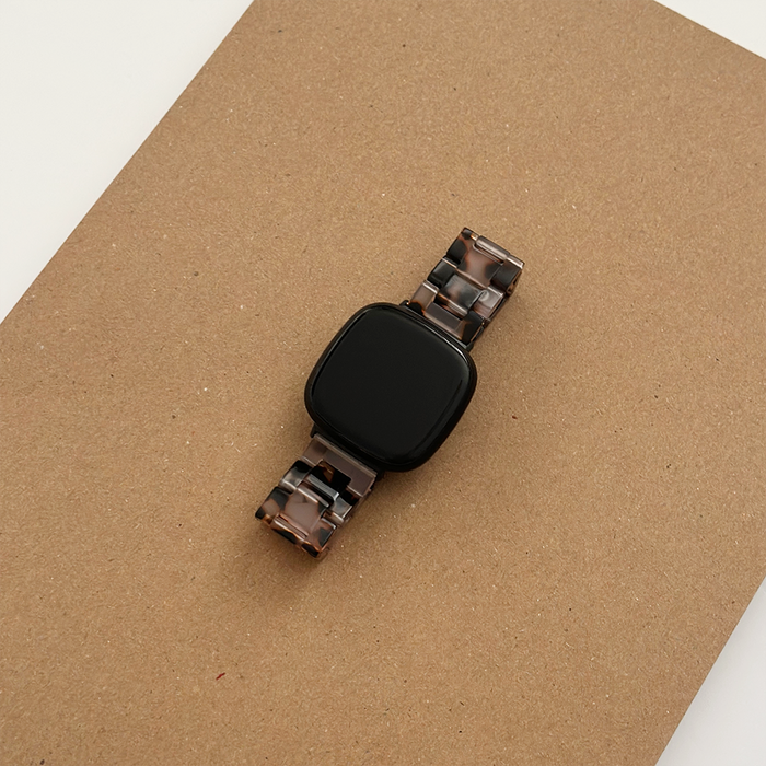 Black square smartwatch with a marbled ivory tortoiseshell strap on a brown surface.