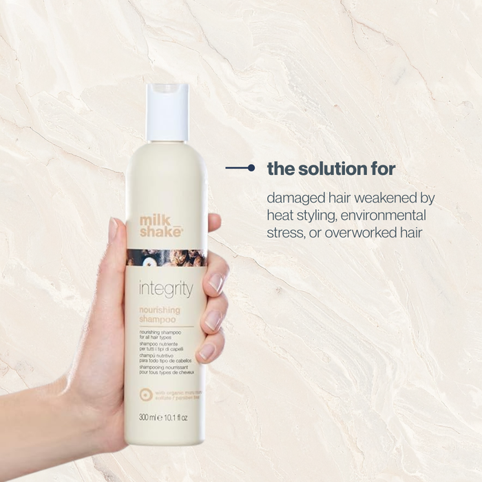 Hand holding a bottle of milk_shake Integrity shampoo against a beige background
