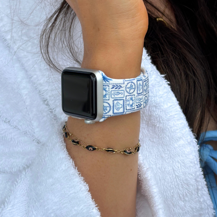 Coconut Lane Malibu Drive Apple Watch strap with pastel pattern on wrist, paired with a gold bracelet and white robe.