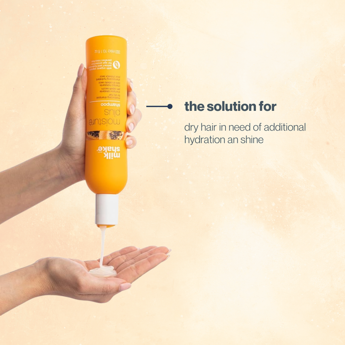 Hand holding a bottle of milk_shake moisture plus shampoo with text on a beige background