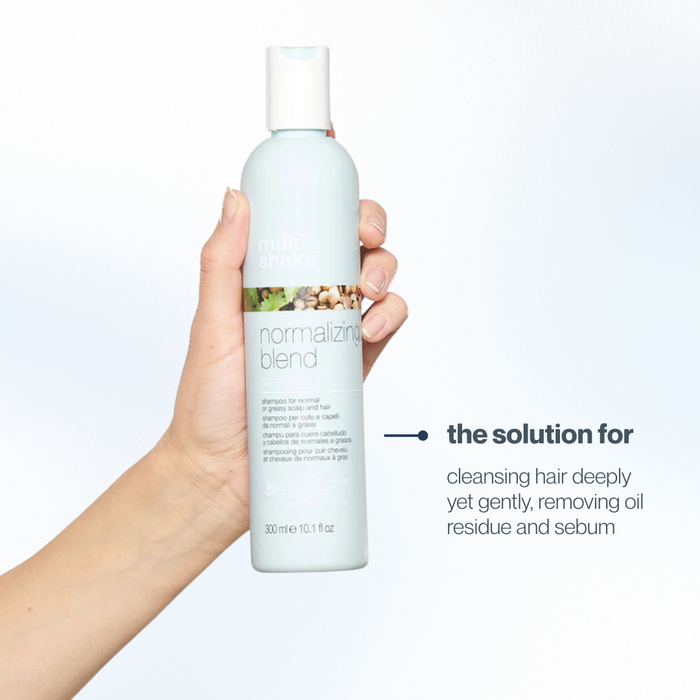Hand holding a bottle of milk_shake  'normalizing blend' shampoo with text on a light gray background