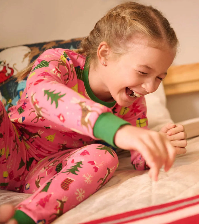 Girl lounging in Hatley Pink Christmas organic cotton pajamas with festive holiday print.