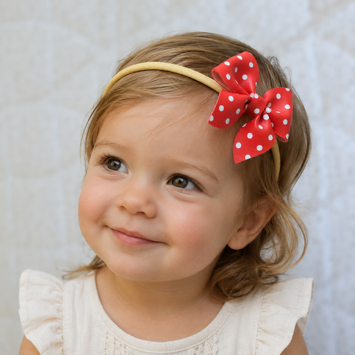 Toddler girl wearing a red polka dot sailor bow headband on a neutral background