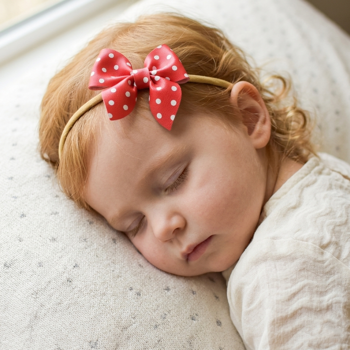 Child sleeping with a red polka dot sailor bow headband, laying on a soft surface