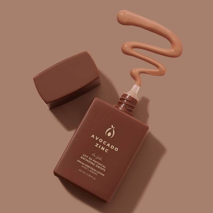 Avocado Zinc bronzer + sunscreen bottle with lid off showing a swatch of product on a brown background