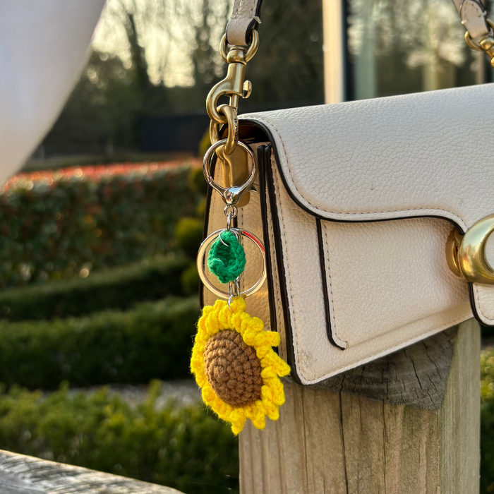 Sunflower bag charm with gold hardware on a white handbag, displayed outdoors in bright sunlight.