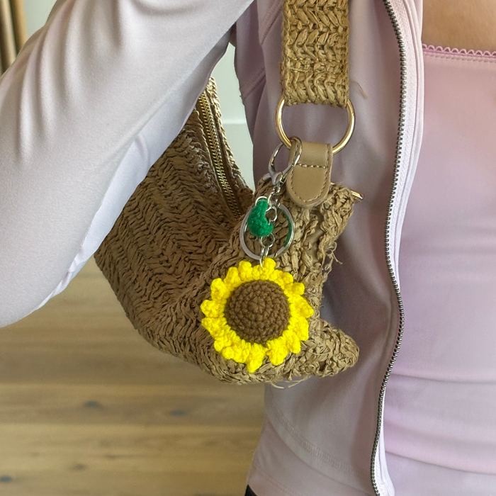 Woven bag with green sunflower bag charm and light pink zip-up top.