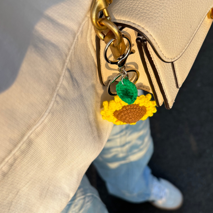 Beige bag with Coconut Lane sunflower charm, paired with light blue jeans and white shoes.