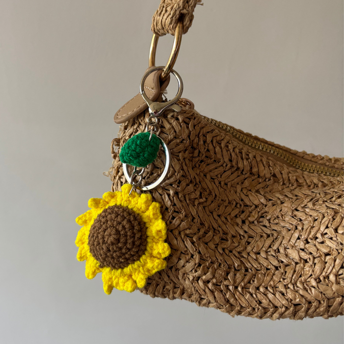 Woven brown bag with a sunflower charm and green leaf accessory attached to the zipper pull.