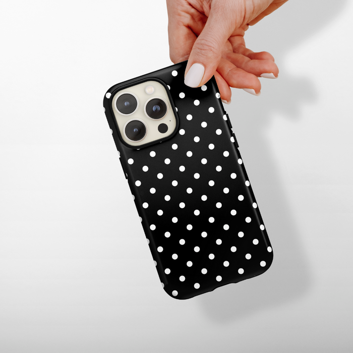 Hand holding a black phone case with white polka dots against a light background.