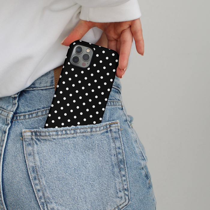 A hand places a black polka dot Coconut Lane tough phone case into the back pocket of blue jeans.