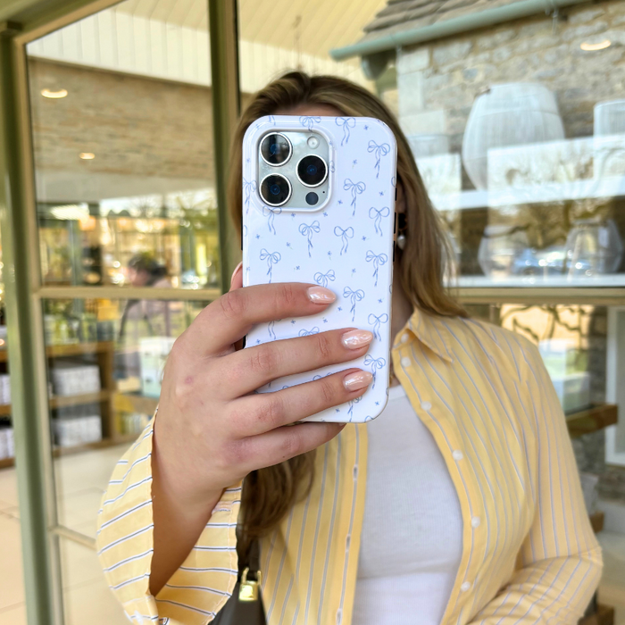 Person in a yellow striped shirt holds a blue phone case with bow pattern near a store window.