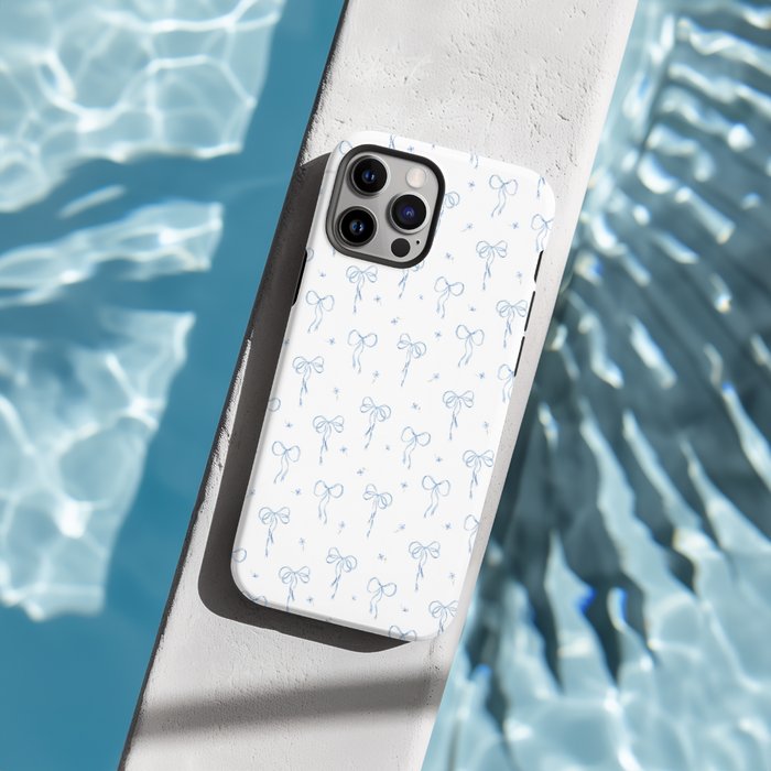 Bluebell Bows blue phone case with bow pattern on a concrete ledge next to a shimmering pool.