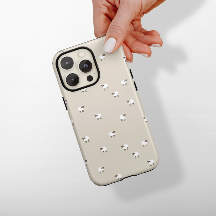 Hand holding a beige Coconut Lane iPhone tough case with a cute sheep illustration.