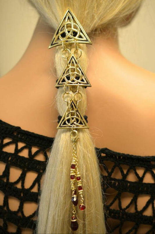 Gold Celtic Trinity Knot Hair Armor ponytail holder worn by model, featuring three linked triangular Celtic knot medallions with dangling bead accents securing a ponytail, rear view.