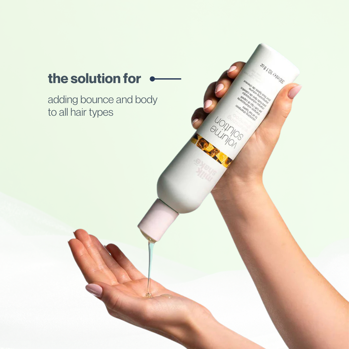 Hand holding a bottle of milk_shake volume shampoo with text on a light green background